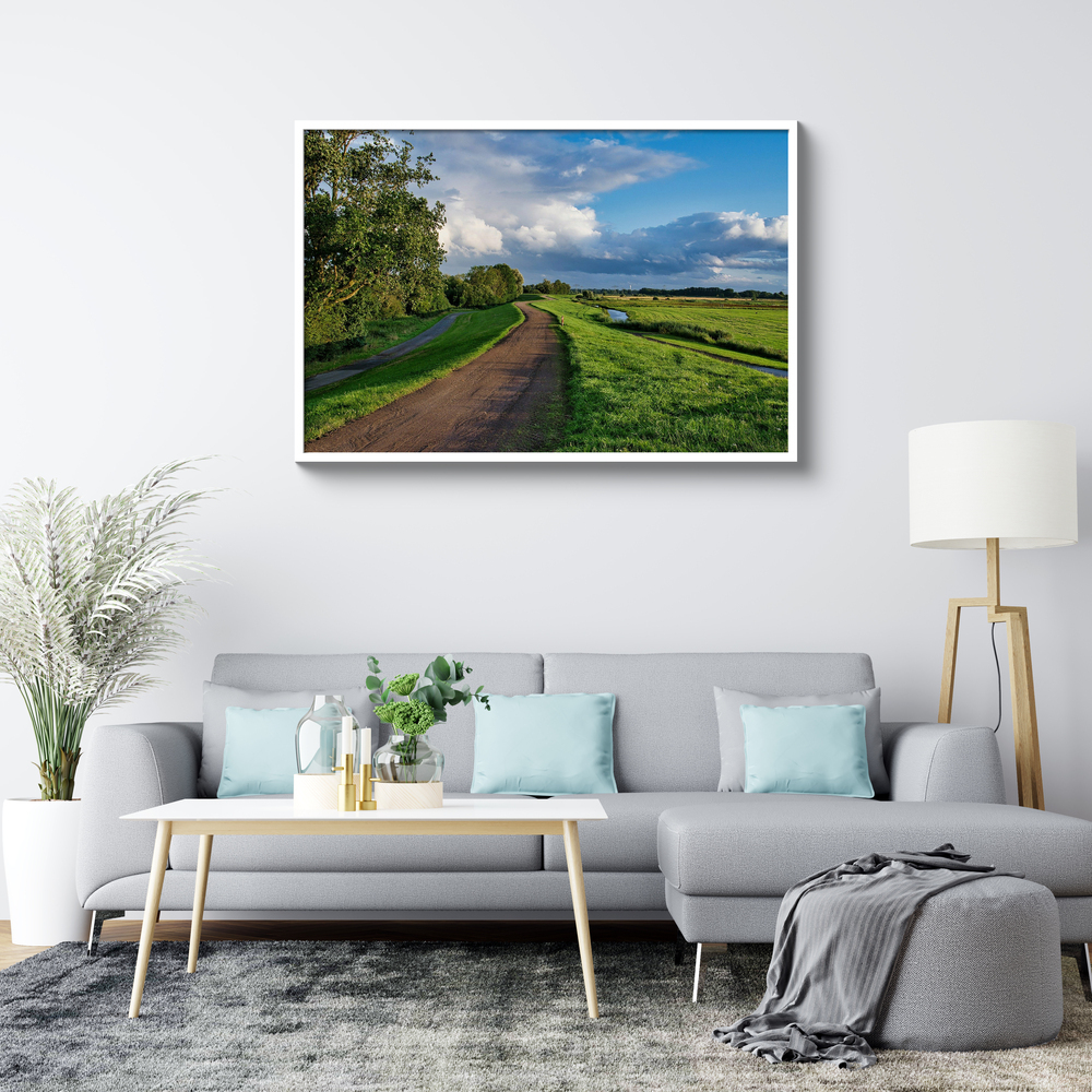 Landschapsfoto op plexiglas in een witte lijst boven een grijze bank in een lichte woonkamer