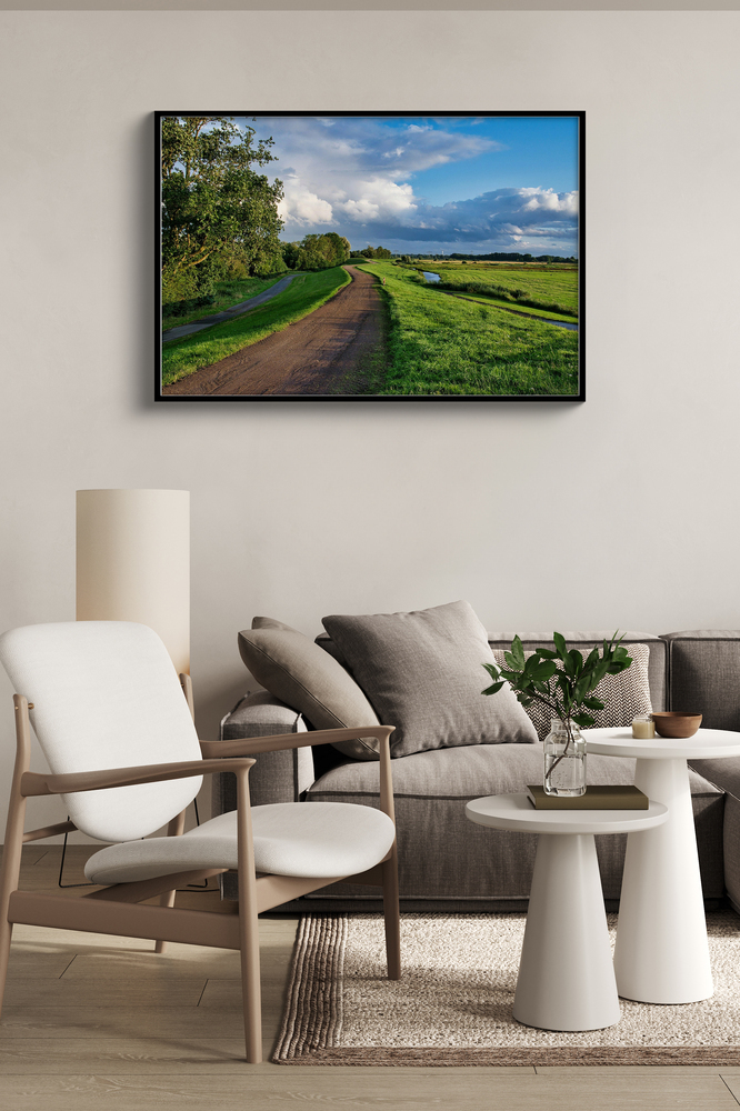 Landschapsfoto op plexiglas in een zwarte lijst boven een bank, naast een lichte fauteuil in de woonkamer