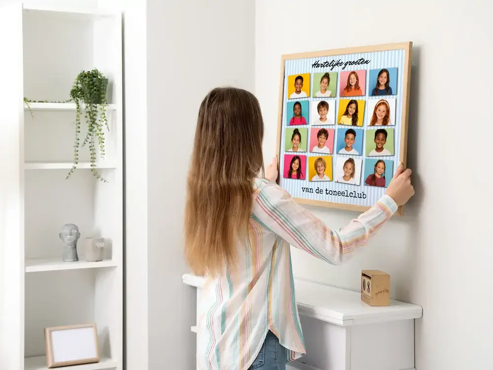Fotocollage van de schooltoneelclub met 16 kinderportretten en een groet, in een houten lijst aan de witte muur