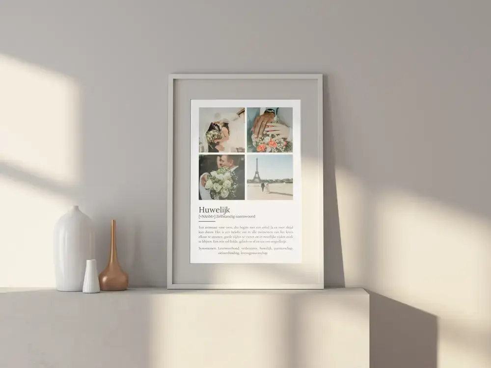 Witte lijst met huwelijksposter in woordenboekstijl en vier trouwfoto’s, op een licht dressoir naast vaasjes