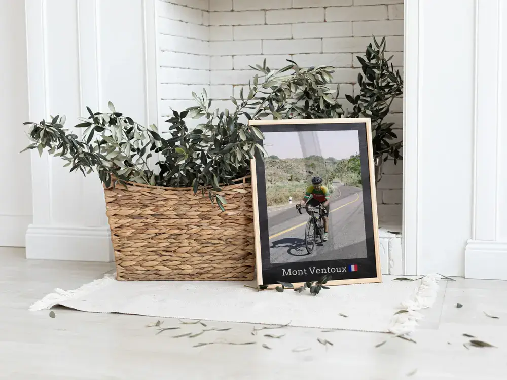 Ingelijste wielrenfoto met plaatsnaam op de vloer naast een plantenmand, als cadeau voor wielrenners