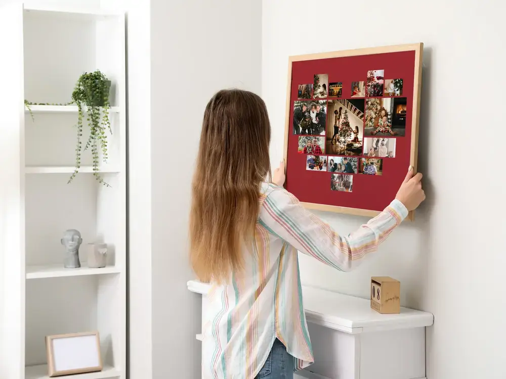 Fotocollage in hartvorm op donkerrood, in een houten lijst aan een lichte muur, als kerstcadeau voor de familie