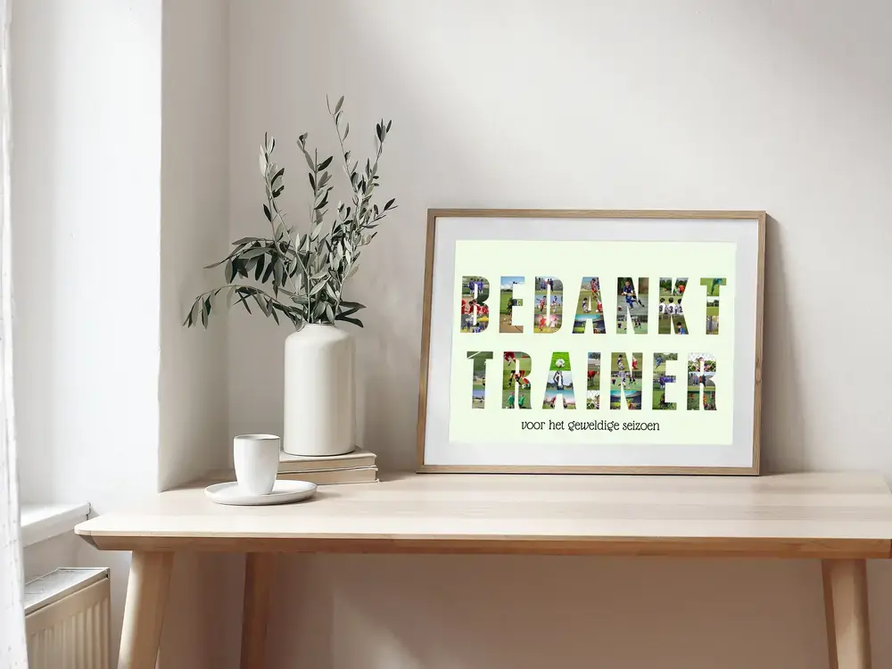 Fotocollage in lettervorm met persoonlijke tekst voor de trainer, in een houten lijst op een bureau naast een vaas