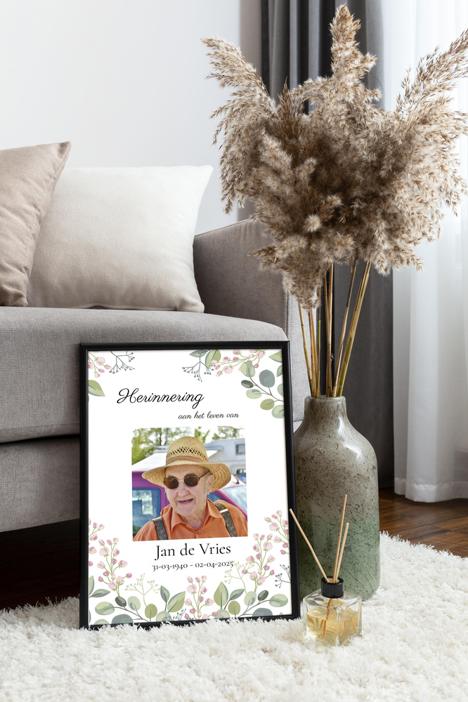 Herdenkingsposter met portret en bloemen in een zwarte lijst, op een vloerkleed naast de bank en een vaas